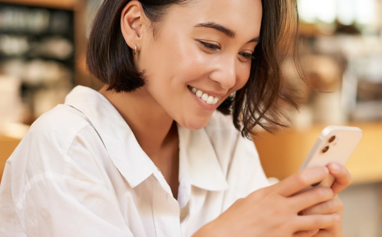 Una mujer sonriente usando su teléfono móvil. Ejemplo de diseño de experiencia de usuario (UX).