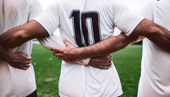 Tres hombres unidos de la mano frente a un campo de fútbol. Imagen relacionada con el diseño de experiencia de usuario (UX).