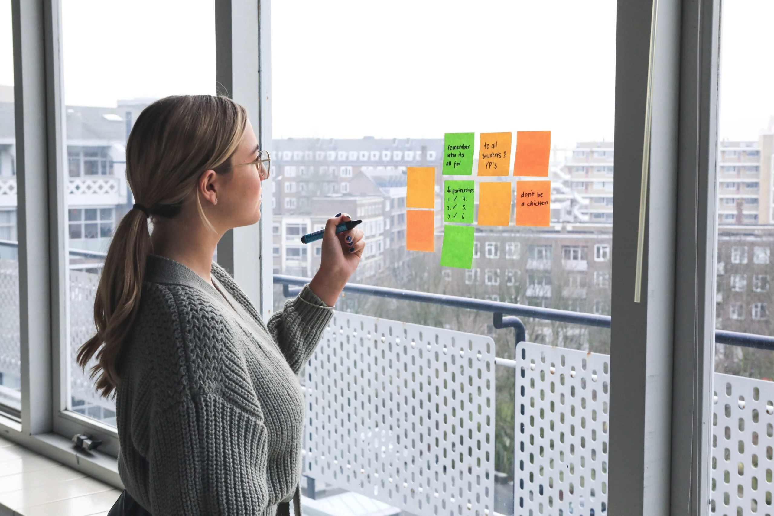 Mujer diseñadora de experiencias definiendo pain points en una nota adhesiva en una ventana.