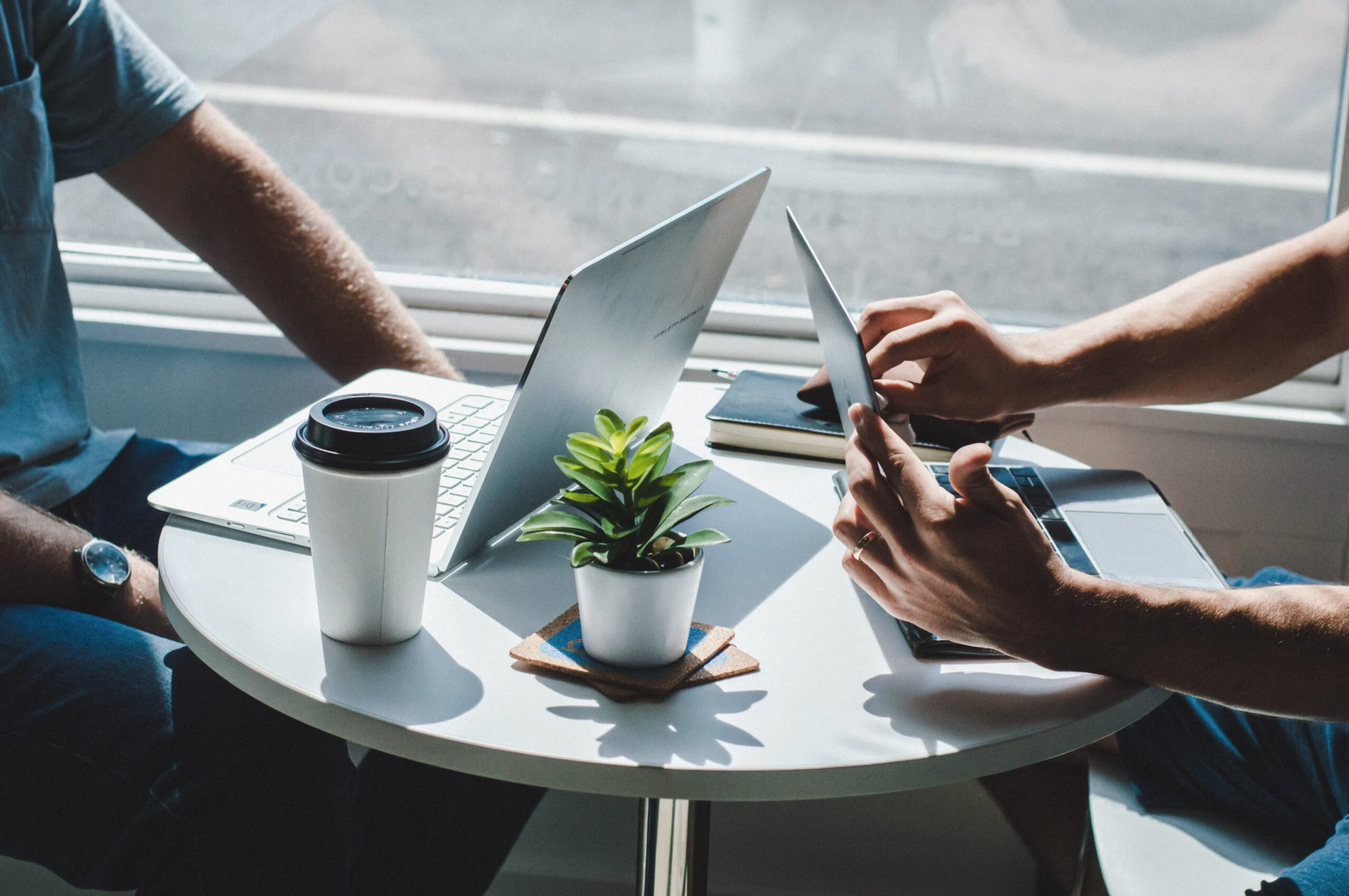 Dos diseñadores UX tomando café y trabajando en sus laptops en una mesa.