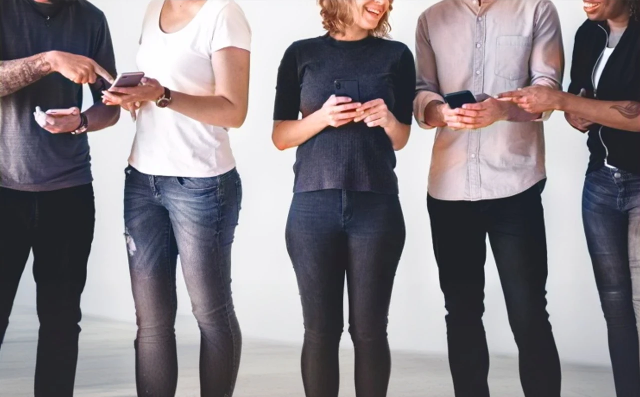 Un grupo de personas de pie en fila mirando sus teléfonos.